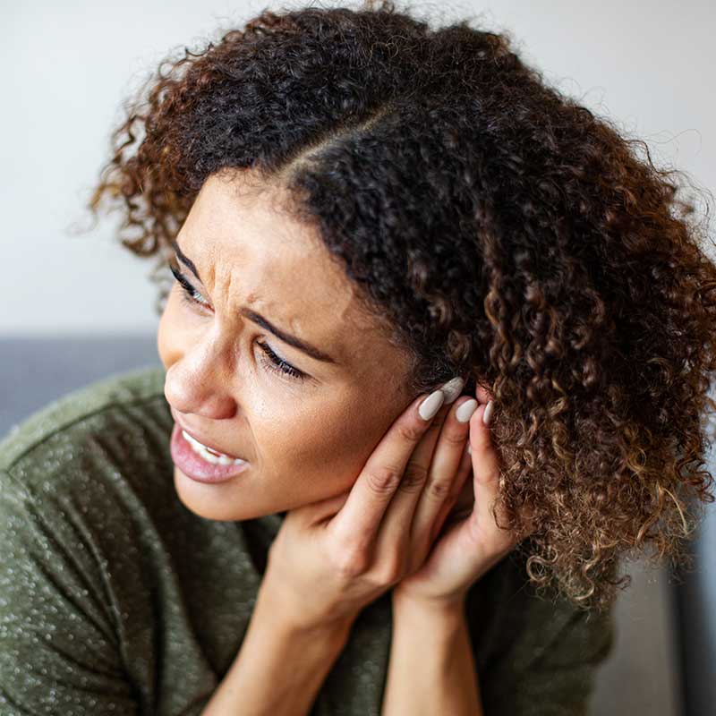 Woman pressing on ears to try to stop the ringing in her ears (tinnitus).