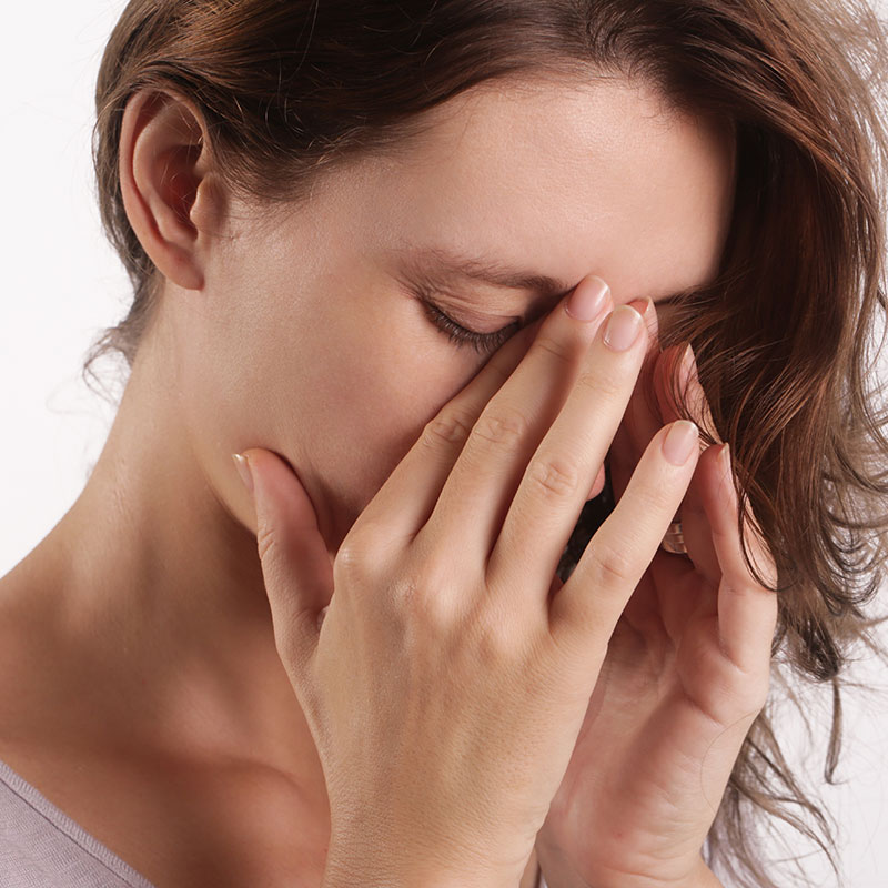 Woman holding the bridge of her nose because she has a deviated septum and is experiencing sinus pain. 
